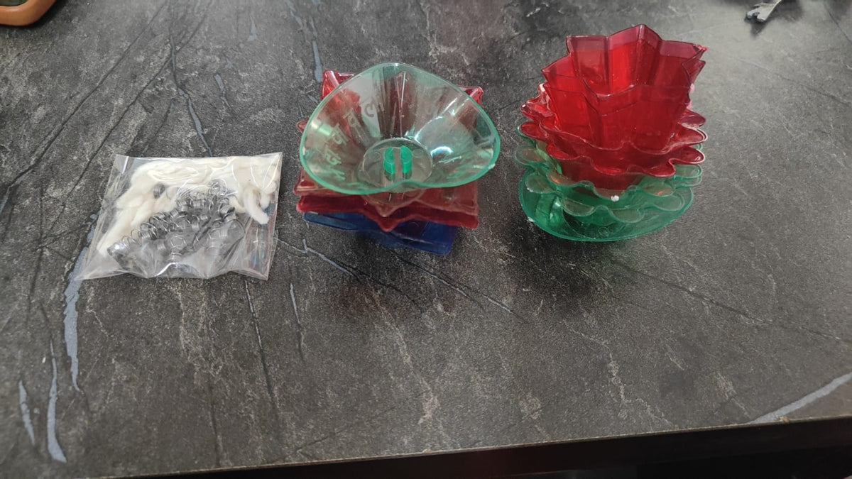 Unlit translucent lotus diyas in red, green and blue stacked beside a pack of wicks