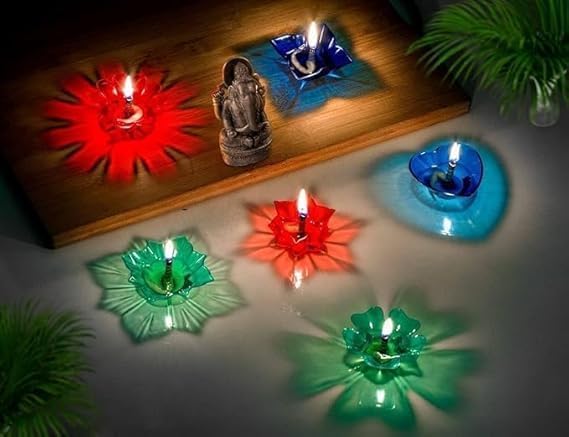 Lit lotus diyas in red, blue and green arranged around a Ganesha idol